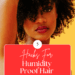 Black woman with naturally curly hair wearing a yellow shirt with a yellow background posing with her hand touching her hair. with text about humidity proof hair for summer weather.